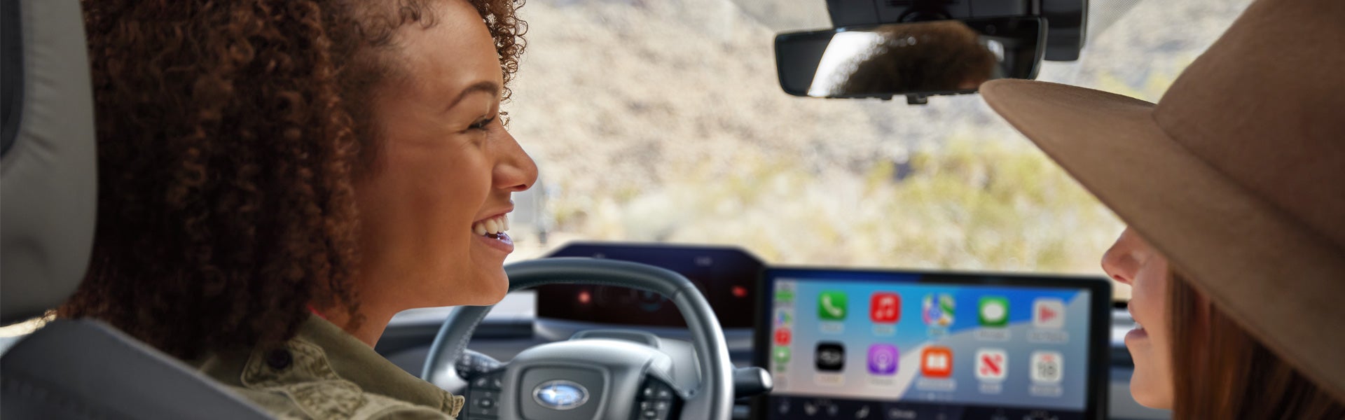 Two women talk in the front seats of a Subaru vehicle.